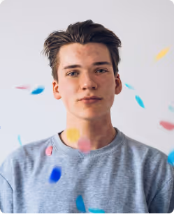 Young man with brown hair wearing a gray shirt with colorful confetti falling around him.