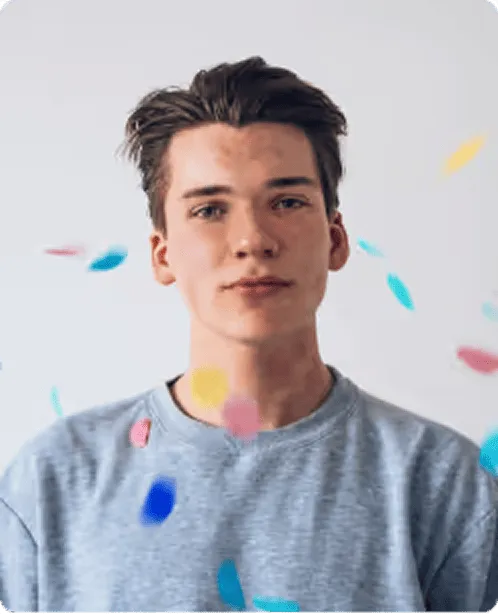 Young man with brown hair wearing a gray shirt with colorful confetti falling around him.