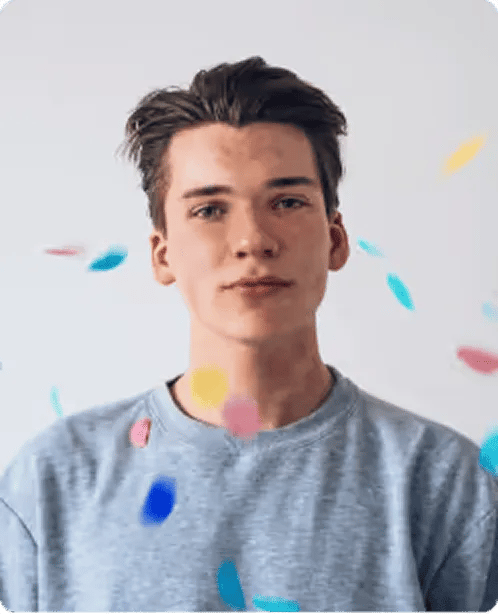 Young man with brown hair wearing a gray shirt with colorful confetti falling around him.