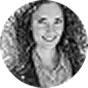 Black and white headshot of a smiling woman with curly hair wearing a plaid shirt and necklace.