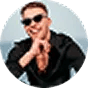 Smiling man wearing sunglasses and a black shirt, making finger gun gestures.
