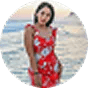 Woman in a red floral dress standing in front of a body of water during sunset.